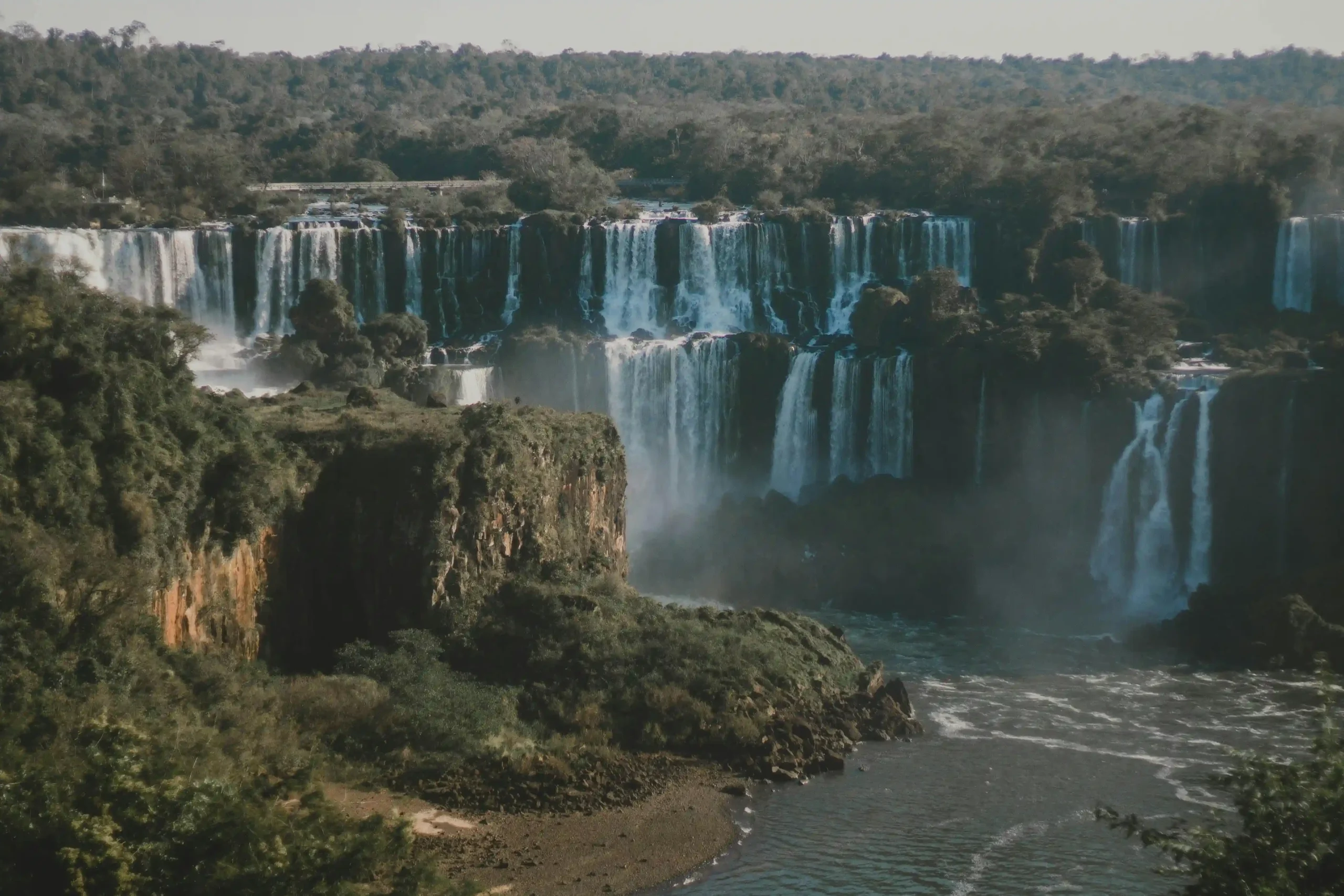 A panoramic view of the mighty Iguazu Falls, showcasing multiple cascades surrounded by lush subtropical rainforest.