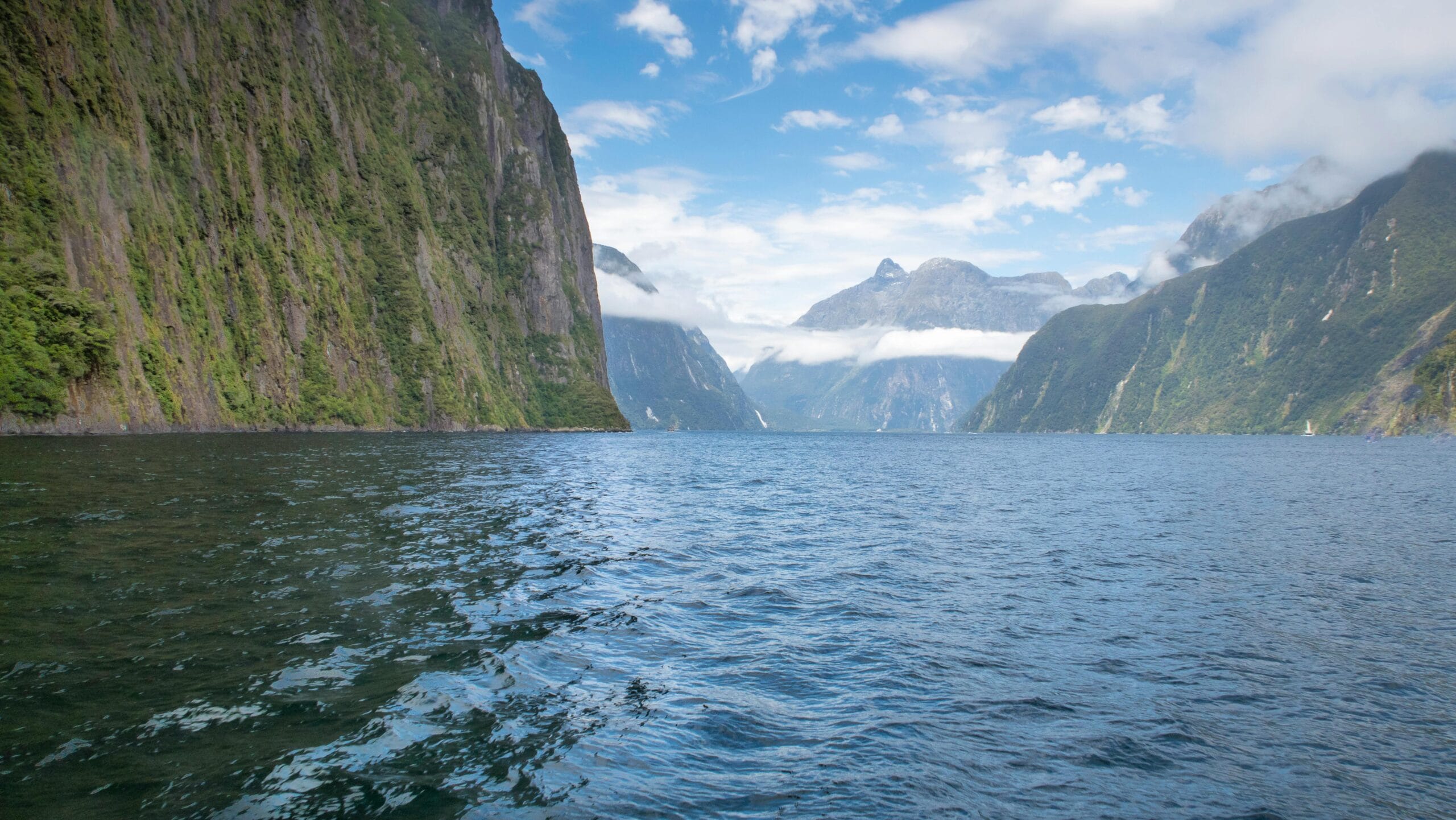 A breathtaking view of New Zealand's Milford Sound, with majestic green fjords rising from dark water.