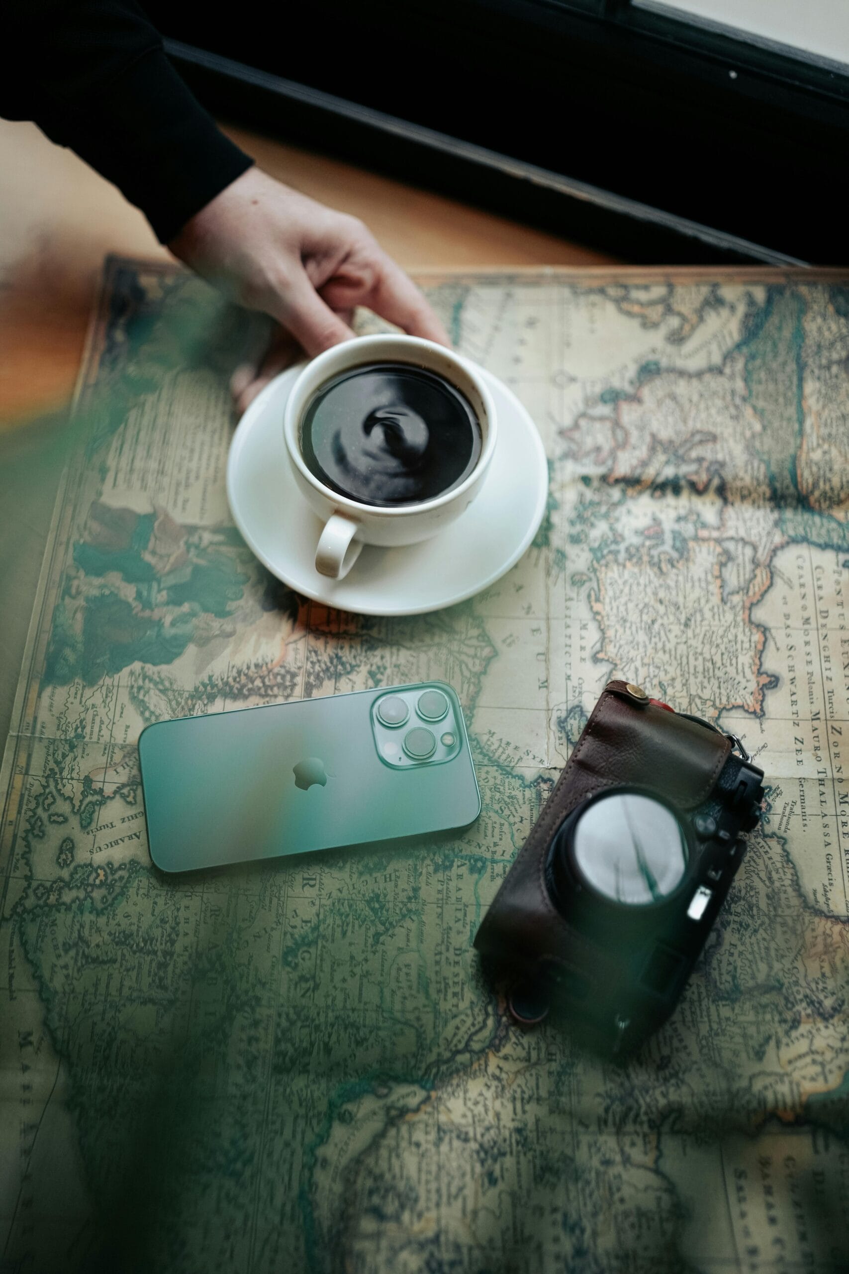 A person planning a trip with a map, coffee, and camera.